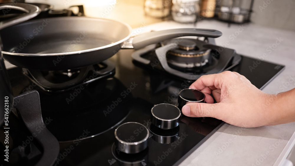 Male hand turning switch knob on modern gas stove in kitchen showroom. Cooking appliance in domestic kitchen. Home improvement and House interior design concepts