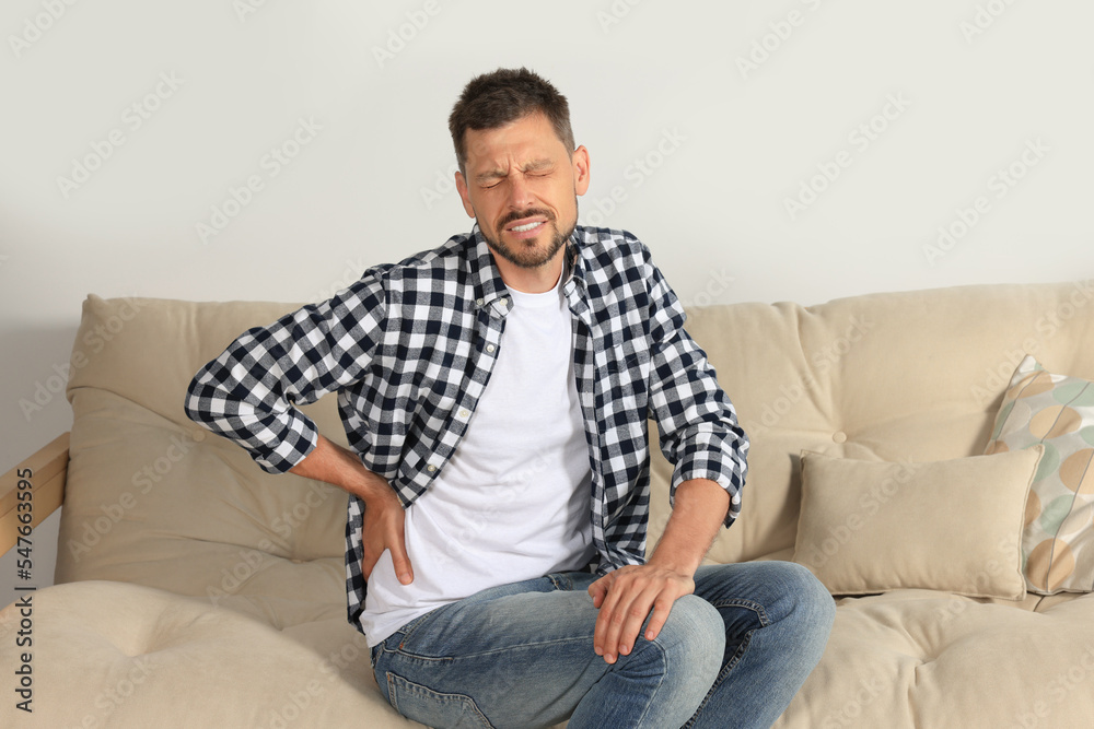 Man suffering from pain in back on sofa at home
