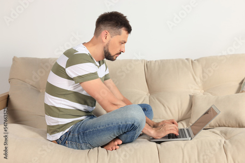 Man with poor posture using laptop on sofa at home © New Africa