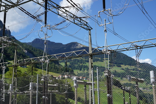 High voltage electricity power distribution plant with cables, expulsion fuses, surge arrester and other components as a part of hydroelectric power plant on reservoir Mapraggsee. Behind are mountains photo