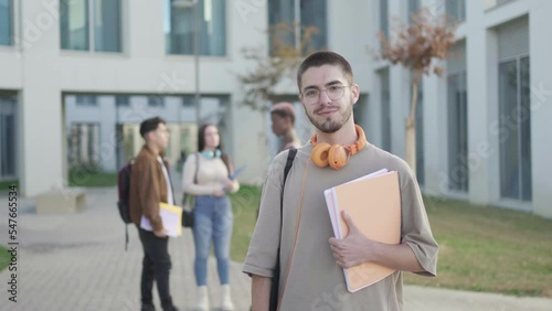 student boy looking at camera while his friends are behind talking, in university campus.
