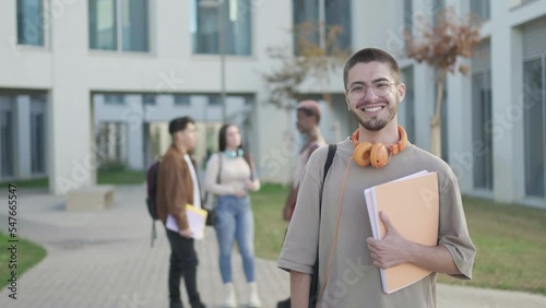 student boy looking at camera while his friends are behind talking, in university campus