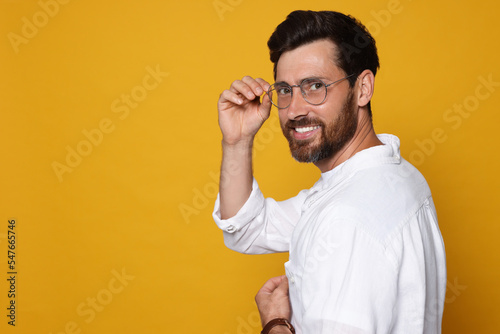 Portrait of smiling bearded man with glasses on orange background. Space for text