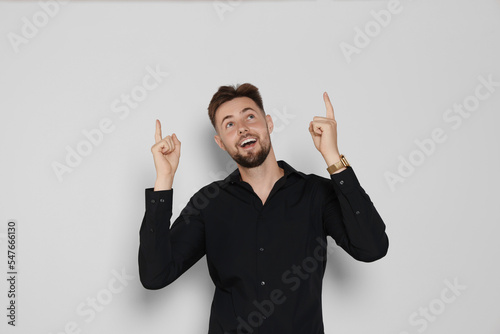 Handsome man in black shirt pointing at something on light grey background