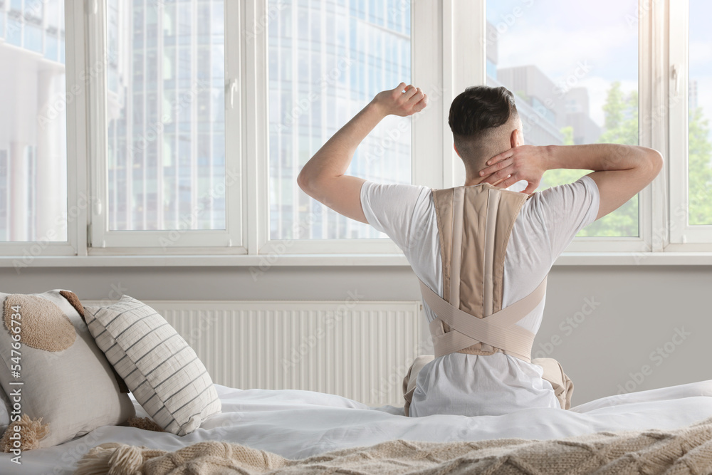Man with orthopedic corset sitting in room, back view Man with orthopedic corset sitting in room, back view