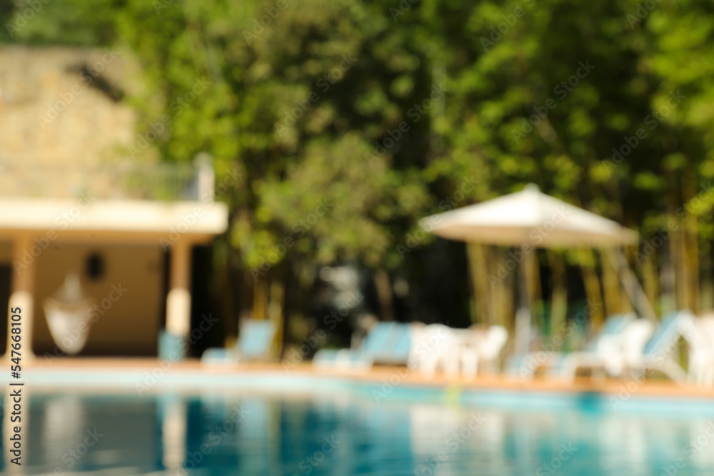 Blurred view of clear pool, sunbeds and umbrella outdoors