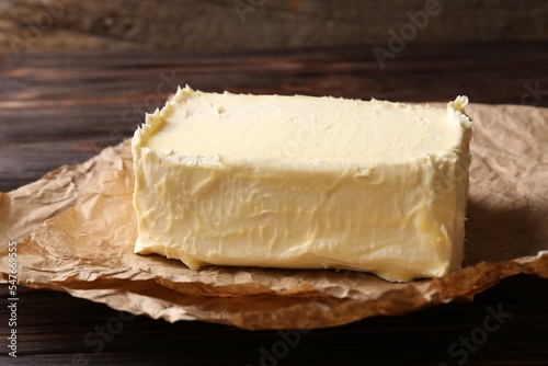 Parchment with piece of tasty homemade butter on wooden table, closeup
