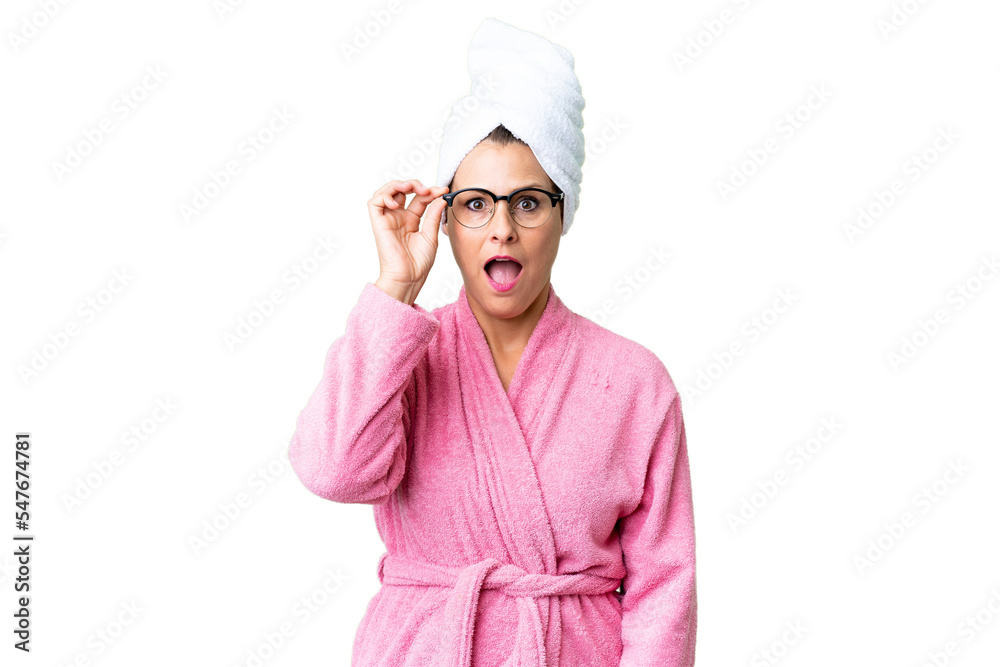 Middle age caucasian woman in a bathrobe over isolated background with glasses and surprised Middle age caucasian woman in a bathrobe over isolated background with glasses and surprised