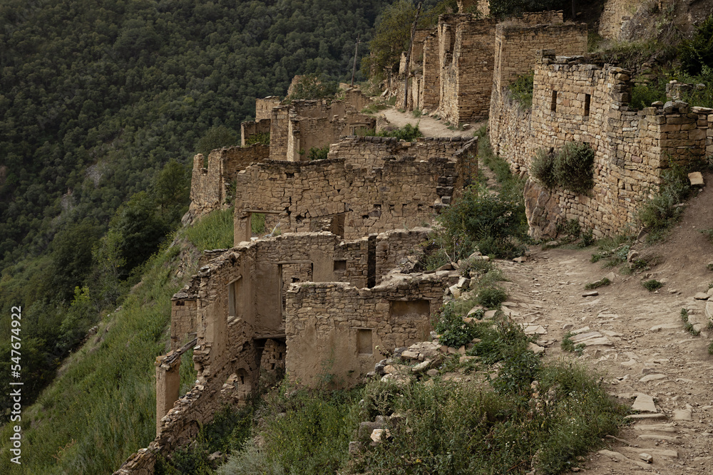 Ancient ruin of stone city in highlands in Dagestan, details of abandoned buildings, street and dirt road on majestic mountains landscape in summer. Breathtaking adventure and travel in mountain.
