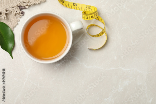 Flat lay composition with herbal diet tea and measuring tape on light marble table, space for text. Weight loss concept