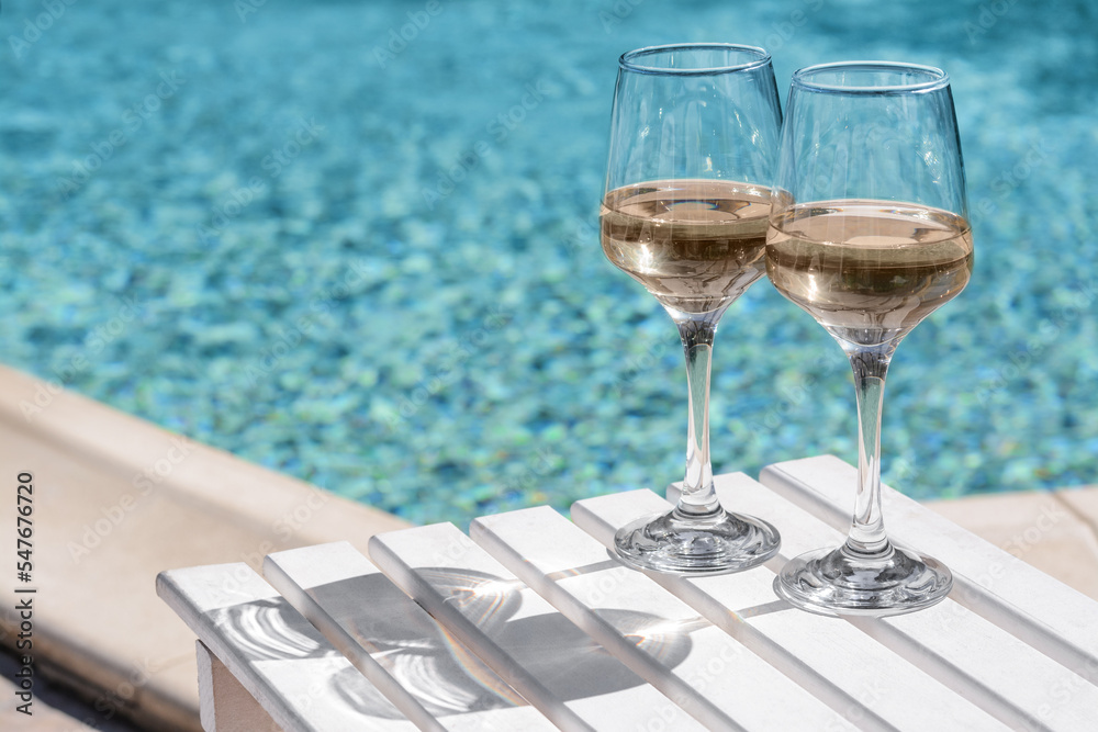 Φωτογραφία Glasses of tasty wine on wooden table near swimming pool, space for text