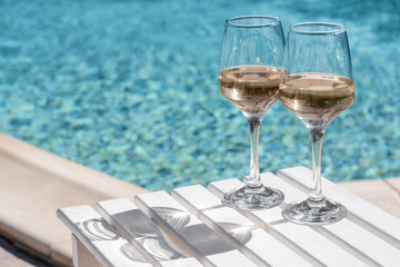 Glasses of tasty wine on wooden table near swimming pool, space for text
