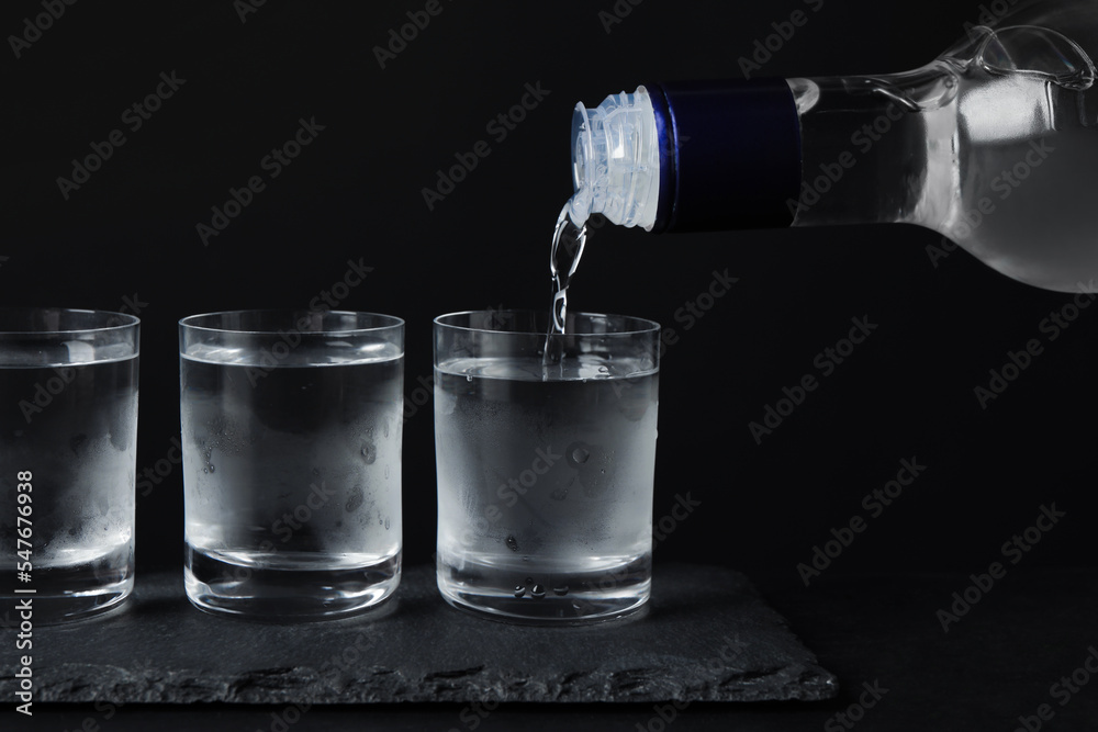 Pouring vodka from bottle in glass on black table Pouring vodka from bottle in glass on black table