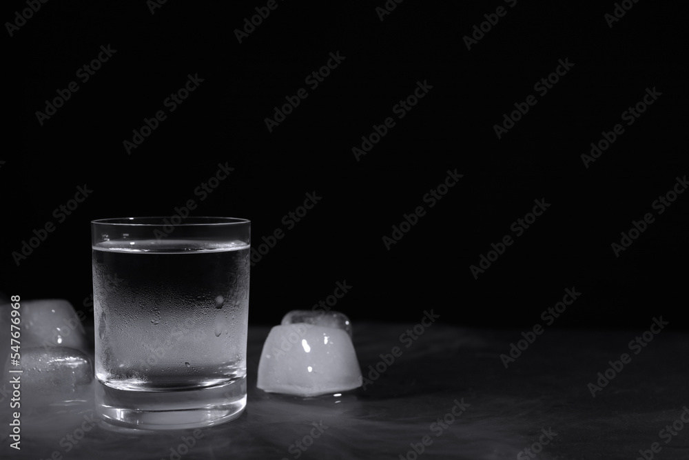 Vodka in shot glass with ice on table against black background Vodka in shot glass with ice on table against black background