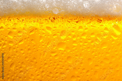 Glass of tasty cold beer with foam and condensation drops as background, closeup