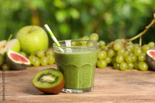 Glass of fresh green smoothie and ingredients on wooden table outdoors, space for text