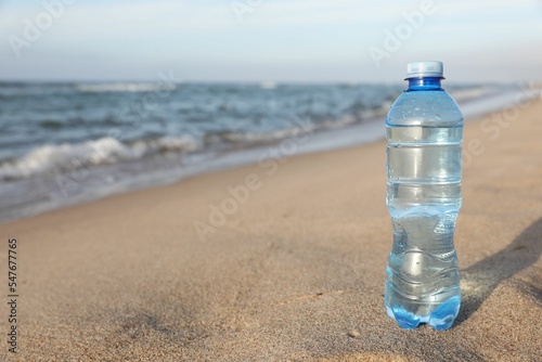 Plastic bottle of fresh water on wet sand near sea. Space for text