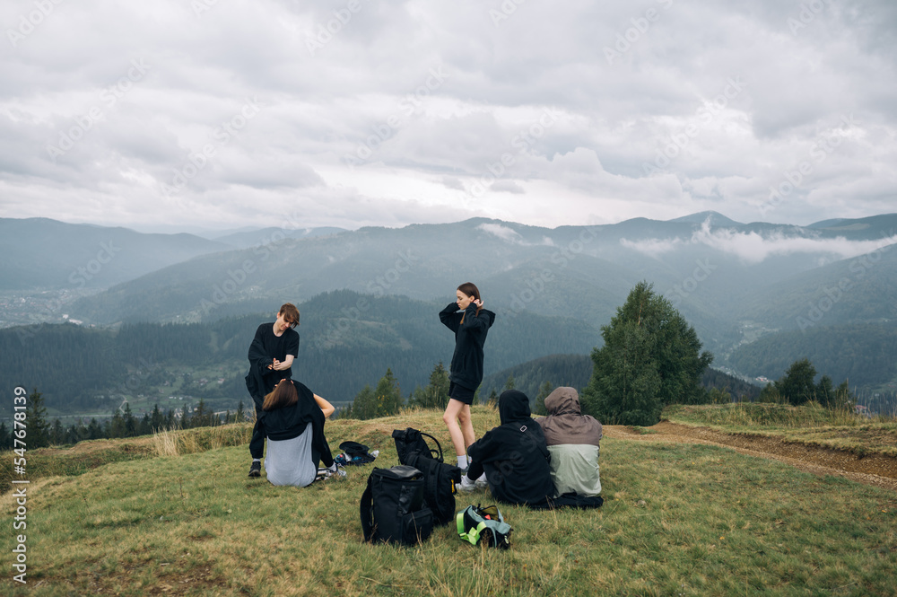Fototapeta premium A group of young people tourists sit in the mountains on the ground in the mountains and rest during the hike against the background of beautiful views of the Carpathians.