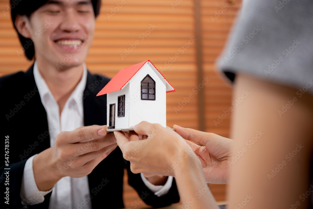 Young realtor man real estate giving house model to hands customer while agreement and contract achievement and approval at home office, investment and mortgage, business and finance concept. Young realtor man real estate giving house model to hands customer while agreement and contract achievement and approval at home office, investment and mortgage, business and finance concept.
