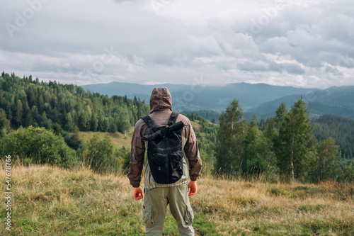 The back of a male tourist with a backpack in the mountains against the background of beautiful views of the Carpathians.