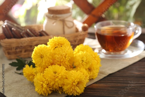 Beautiful yellow chrysanthemum flowers, cup of aromatic tea and sweet chocolate treats on wooden table
