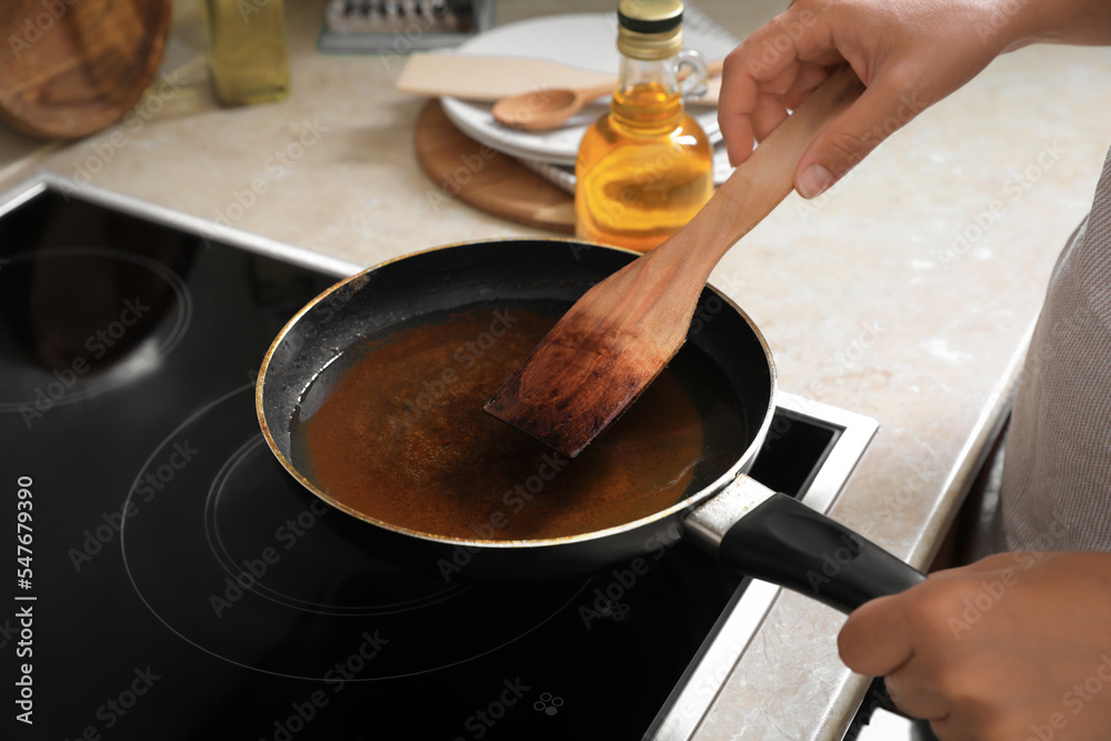 Woman with wooden spatula and frying pan of used cooking oil near stove, closeup Woman with wooden spatula and frying pan of used cooking oil near stove, closeup