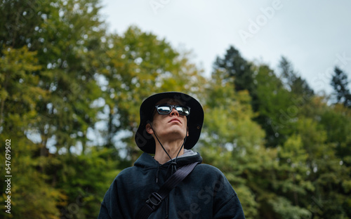 Close-up photo of a male tourist in panama and sun glasses on a background of trees looking up. © bodnarphoto