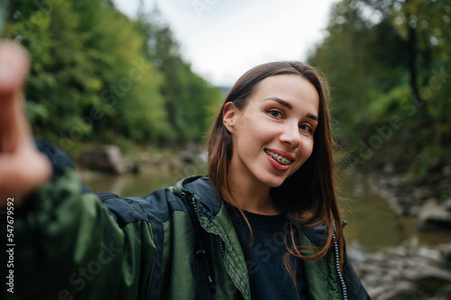 Happy female tourist in the mountains taking a selfie with a smile on her face against the background of a fast mountain river