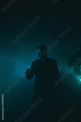 Cinematic night photo in the fog in the blue light, looking away with a serious face.