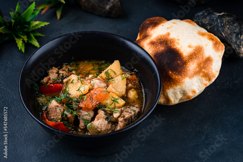 Fresh stewed pork with potatoes, sweet peppers, tomatoes, onions in tomato sauce with herbs and flatbread in a bowl. photo