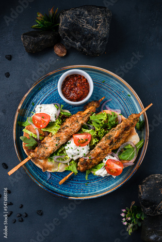 Kebab, barbecued chicken on a stick with tomatoes, lettuce, onion, arugula, sour cream, tortilla and red sauce.