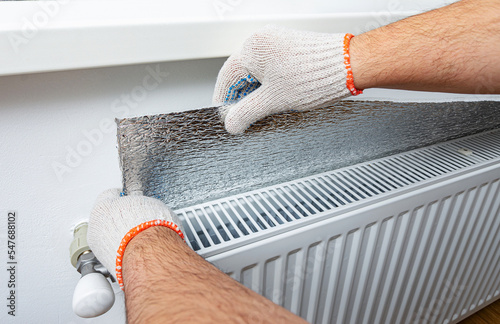 Installation of an energy efficient polythene film of aluminum foil thermal insulation on the wall, behind the heating radiator at home. Thermal insulation, saving money, energy saving.