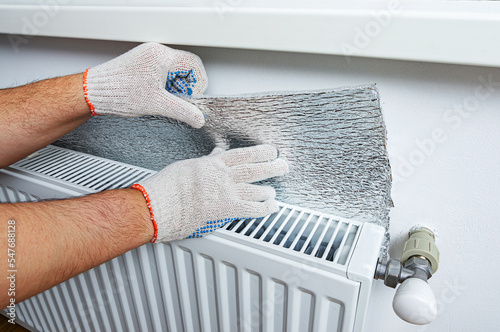 Installation of a polythene bubble film of aluminum foil thermal insulation on the wall behind the heating radiator at home. Thermal insulation of the apartment, saving money on home heating.