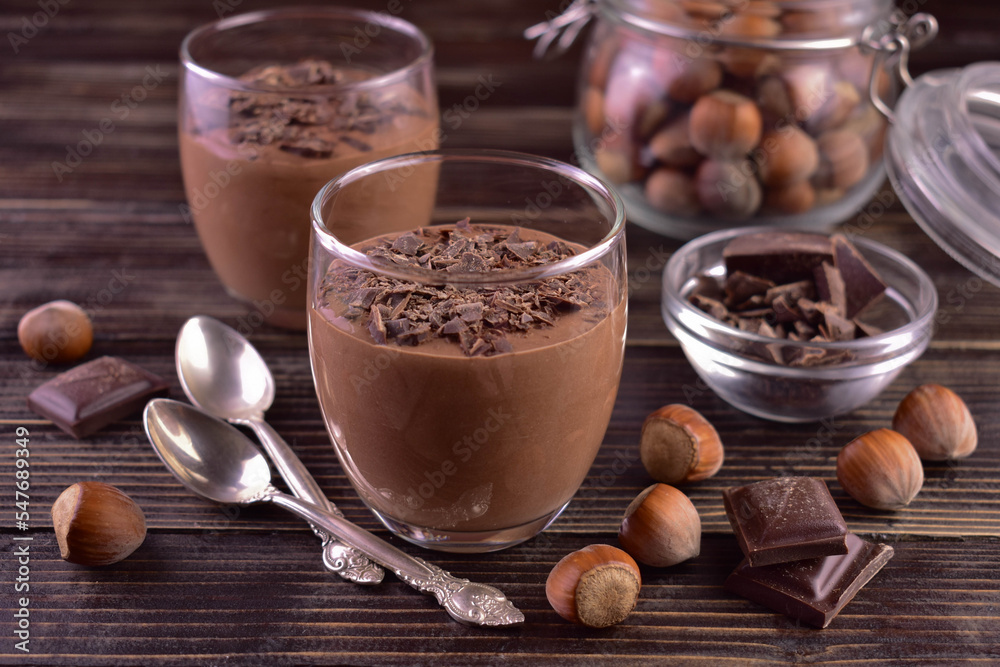 Chocolate mousse with hazelnuts in glasses on a dark wooden background.
Chocolate mousse with hazelnuts in glasses on a dark wooden background.