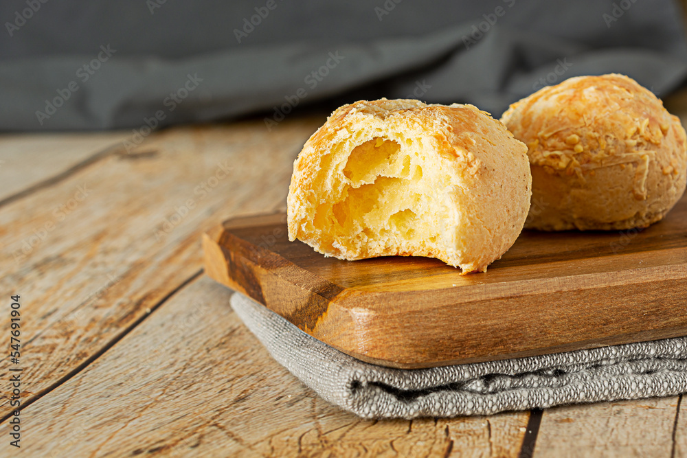 bitten pão de queijo, a traditional brazilian food made of chesse bread, over wooden table and cutting board