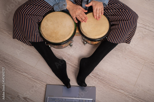 A faceless woman sits on the floor at home and watches educational videos of playing mini bongs. Girl remotely learns to play traditional ethnic drums.