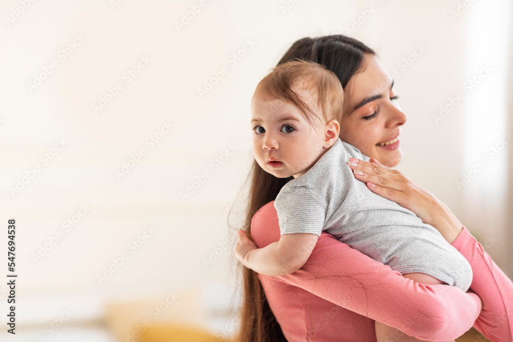 Young mom holding and hugging adorable baby, enjoying motherhood and child care, standing in bedroom at home Young mom holding and hugging adorable baby, enjoying motherhood and child care, standing in bedroom at home