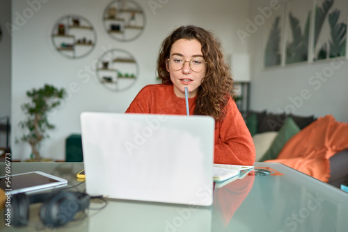 Young woman female student using laptop elearning or remote working at home office looking at computer watching webinar, learning training, studying online seminar or video calling for work meeting. photo