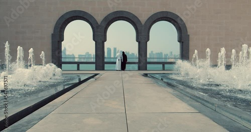 Man and woman standing below arches with Doha skyline. photo