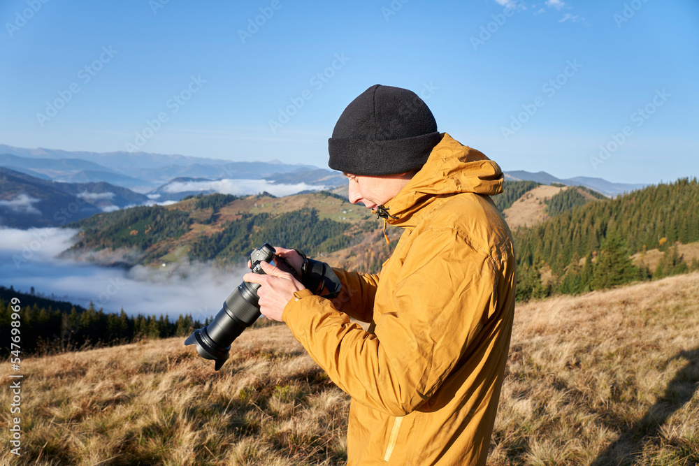 Fototapeta premium Photographer working outdoor. Taking photos in mountains. Nature photographer in action. Silhouette of a landscape photographer in twilight.