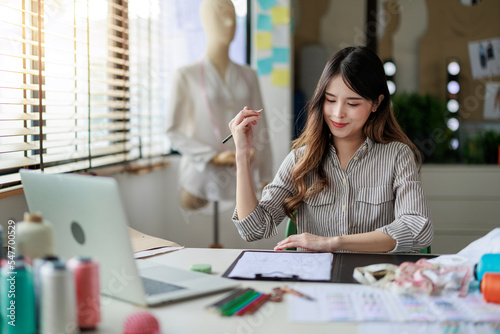 A young beautiful asian cloth designer working at her design table. She is drawing her new design on a paper.