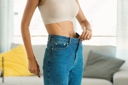 Slim young lady in too big jeans showing how she losing weight, eating healthy food and working out, free space photo