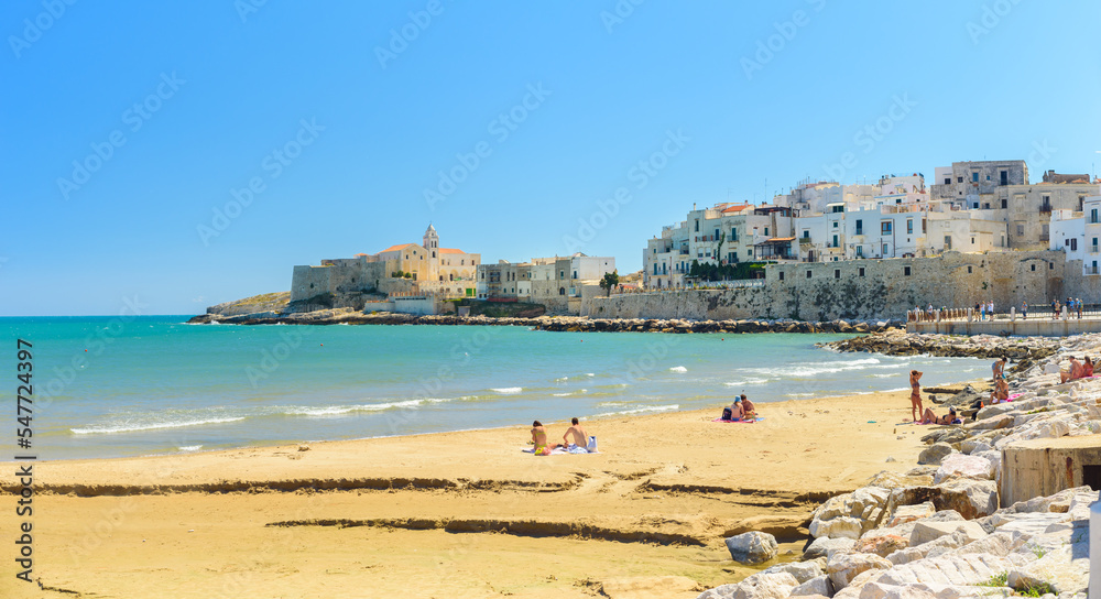 Vieste, Italy. View of the town with the beach of the Lungomare Cristoforo Colombo with some people. In the distance the Church of San Francesco. September 5, 2022.