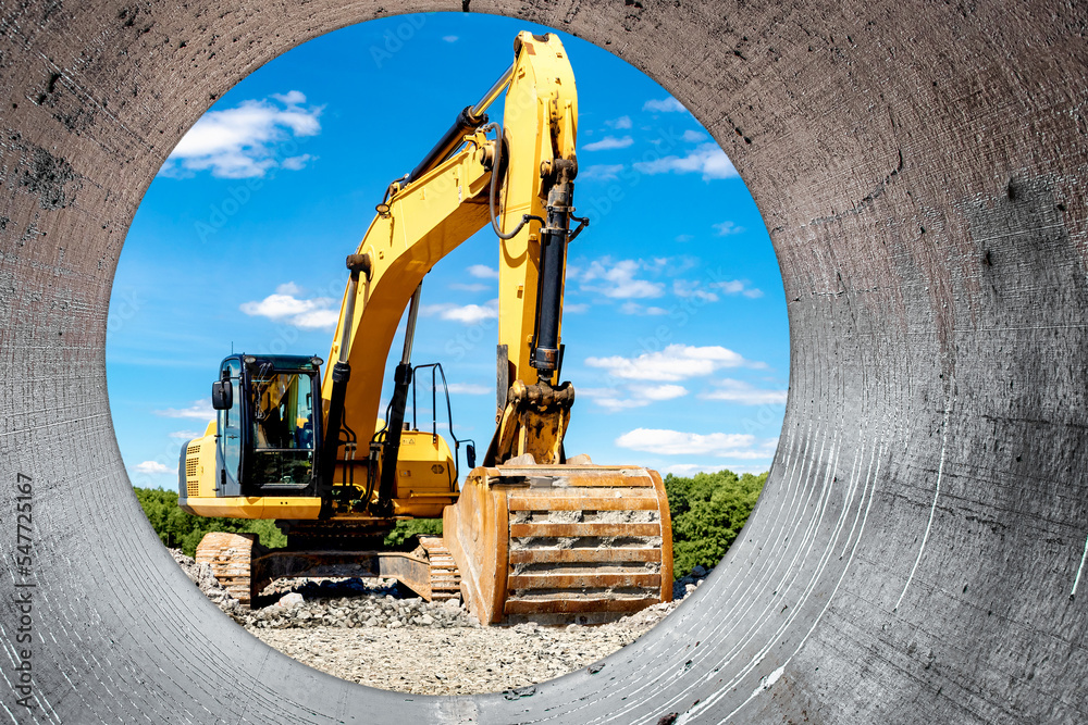 Powerful excavator at the construction site. View of the excavator through the pipe. Close-up of earthmoving machinery. Construction equipment for earthworks. Soil development.