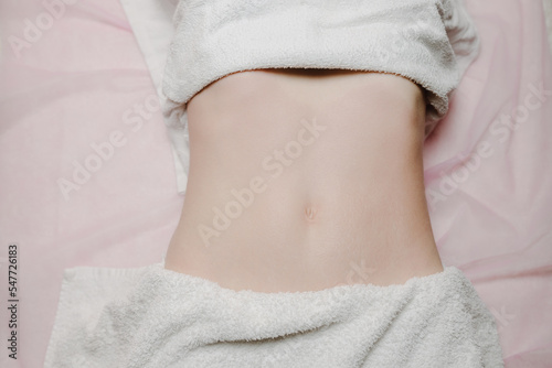  Belly of a young European woman on a massage bed. Preparation for procedures. Professional abdominal massage. Top view