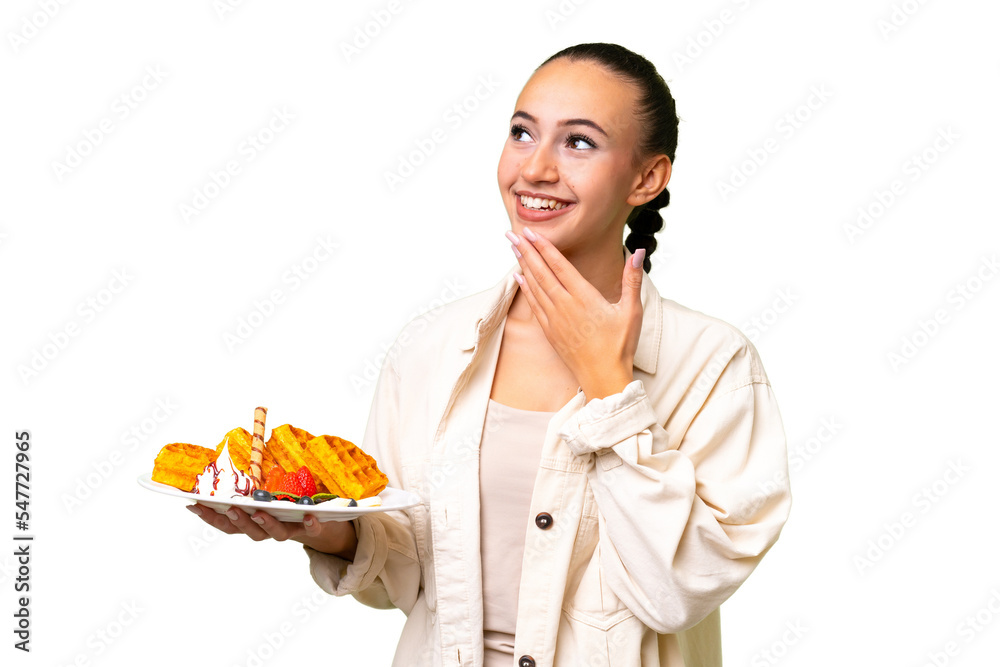 Young Arab woman holding waffles over isolated background looking up while smiling Young Arab woman holding waffles over isolated background looking up while smiling