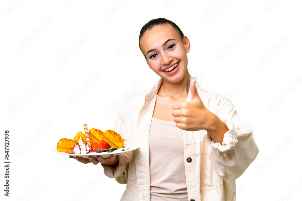 Young Arab woman holding waffles over isolated background with thumbs up because something good has happened Young Arab woman holding waffles over isolated background with thumbs up because something good has happened