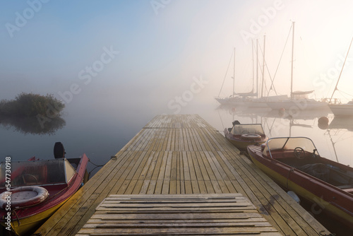 Foggy morning in small river port with anchored sailboats and motorboats