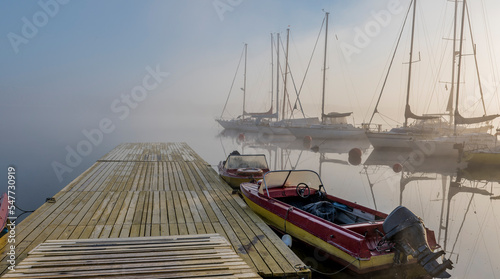 Foggy morning in small river port with anchored sailboats and motorboats