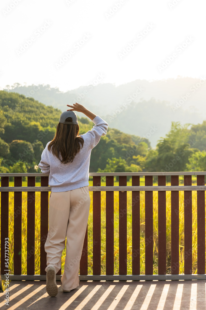 Woman traveler stand at terrace in the natural resort or hotel style to sightseeing paddy field on mountain background.Bak view of young girl enjoying beauty of nature looking at mountain.